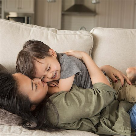 simsearch:6118-07966891,k - A woman lying on a sofa, smiling, cuddling her young son. Photographie de stock - Premium Libres de Droits, Code: 6118-08202583