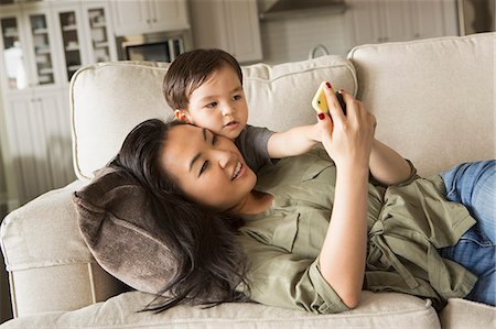 simsearch:6118-07966891,k - Woman lying on a sofa, smiling, cuddling with her young son and looking at a cell phone. Photographie de stock - Premium Libres de Droits, Code: 6118-08202580