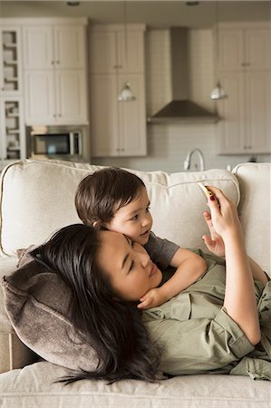 simsearch:6118-07966891,k - Woman lying on a sofa cuddling with her young son and looking at a cell phone. Photographie de stock - Premium Libres de Droits, Code: 6118-08202581