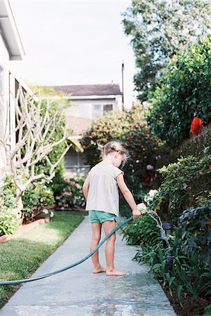 playing with hose - Young girl standing on a path in a garden, playing with a water hose. Stock Photo - Premium Royalty-Free, Code: 6118-08202501