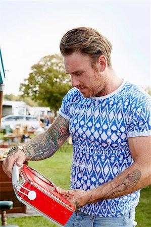 Man with tattoos looking at a red vintage radio at a flea market. Foto de stock - Royalty Free Premium, Número: 6118-08202535