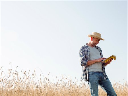 A man in working clothes, jeans and straw hat, using a digital tablet standing in a cornfield. Photographie de stock - Premium Libres de Droits, Code: 6118-08220612