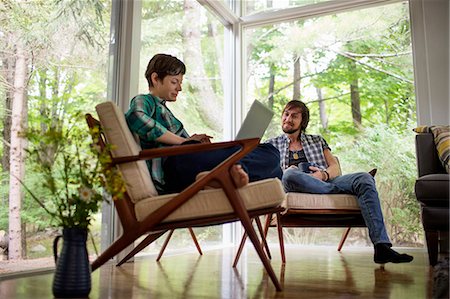 simsearch:6118-08226978,k - A man and woman sitting together in a room with large picture windows, one using a laptop. Foto de stock - Sin royalties Premium, Código: 6118-08226940