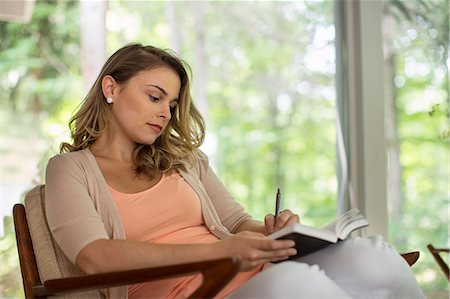 A woman seated holding an open journal and a pen. Stock Photo - Premium Royalty-Free, Code: 6118-08226948