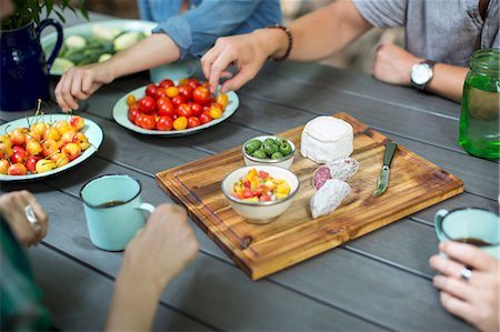 A group of people gathered around a table with plates of fresh fruits and vegetables, and a round cheese and salami on a chopping board. Foto de stock - Sin royalties Premium, Código: 6118-08226908