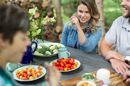 family and meal - Three people seated at a table outdoors, with fresh fruit and vegetables in plates on the table. Stock Photo - Premium Royalty-Free, Code: 6118-08226909