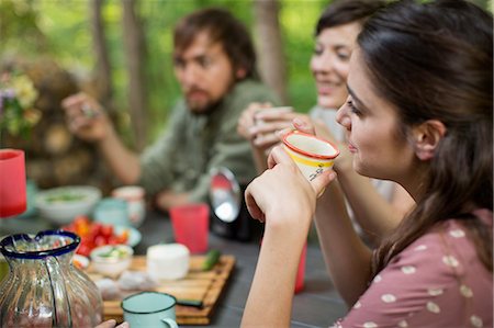 Four people seated around a wooden table outdoors in woodland sharing a meal. Stock Photo - Premium Royalty-Free, Code: 6118-08226922