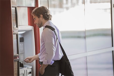 A man with a laptop bag using an ATM, a cash machine on a city street. Stock Photo - Premium Royalty-Free, Code: 6118-08351845