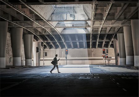 simsearch:6118-08351888,k - A person crossing an open space, a city underpass, with concrete walls and a pool of sunlight. Foto de stock - Royalty Free Premium, Número: 6118-08351849