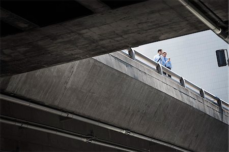 simsearch:6118-08351863,k - Two businessmen standing leaning on a railing on a city walkway, view from below. Stock Photo - Premium Royalty-Free, Code: 6118-08351853