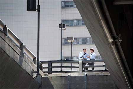 simsearch:6118-08351860,k - Two businessmen standing leaning on a railing on a city walkway, view from below. Stock Photo - Premium Royalty-Free, Code: 6118-08351852