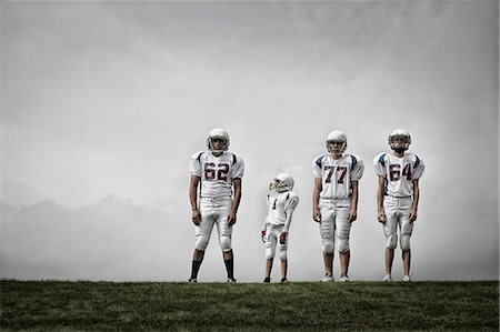 football practice - A group of four football players in sports uniform, three tall figures and one shorter team player. Stock Photo - Premium Royalty-Free, Code: 6118-08351823