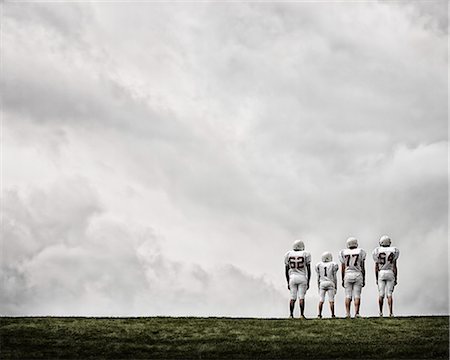 people walking in line side view - A group of four football players in sports uniform, three tall figures and one shorter team player. Stock Photo - Premium Royalty-Free, Code: 6118-08351821