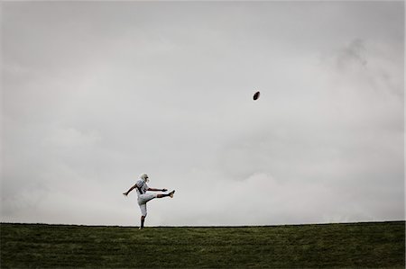 A football player in uniform, side view, practicing his kicking. Ball in mid air. Stock Photo - Premium Royalty-Free, Code: 6118-08351825