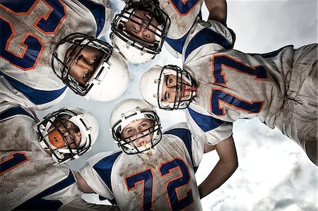 footballeur (sport américain) - A group of football players, young people in sports uniform and protective helmets, in a team huddle viewed from below. Photographie de stock - Premium Libres de Droits, Code: 6118-08351829