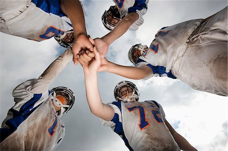 A group of football players, young people in sports uniform and protective helmets, in a team huddle viewed from below. Stock Photo - Premium Royalty-Free, Code: 6118-08351830