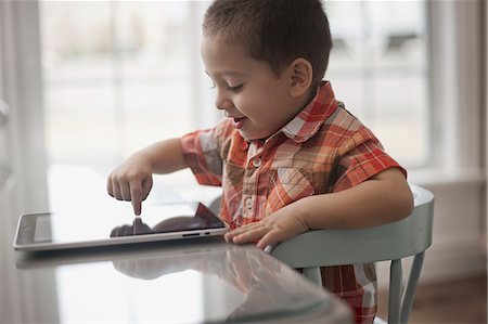 simsearch:6118-08660001,k - A young child sitting at a table using a digital tablet with a touchscreen. Stock Photo - Premium Royalty-Free, Code: 6118-08351993