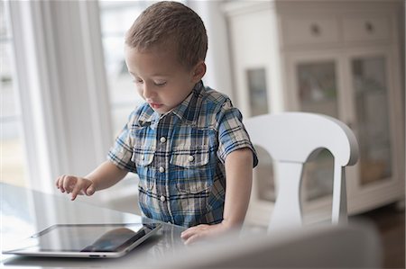 simsearch:6108-05867616,k - A young child sitting at a table using a digital tablet with a touchscreen. Stock Photo - Premium Royalty-Free, Code: 6118-08351991