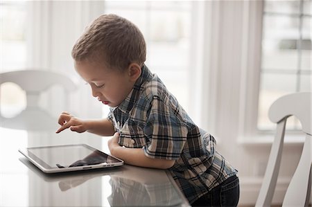 simsearch:6108-05867616,k - A young child sitting at a table using a digital tablet with a touchscreen. Stock Photo - Premium Royalty-Free, Code: 6118-08351992