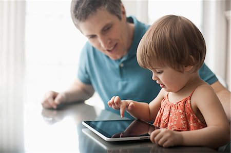 A man and a young child sitting looking at a digital tablet and touching the screen. Stock Photo - Premium Royalty-Free, Code: 6118-08352008