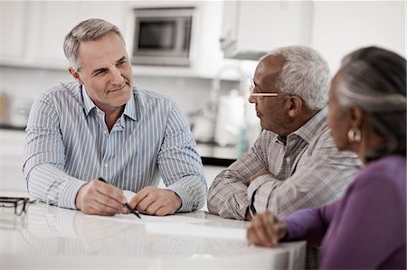 Three people at a table, a senior couple seated with a man using paper and pen to give them information. Fotografie stock - Premium Royalty-Free, Codice: 6118-08393955