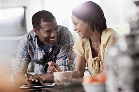 A man and woman, couple in ther kitchen both looking at a digital tablet. Stock Photo - Premium Royalty-Free, Code: 6118-08393960