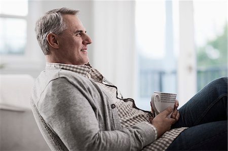 A mature man with grey hair leaning back in a chair, relaxing with a cup of tea or coffee. Stock Photo - Premium Royalty-Free, Code: 6118-08393978