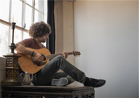 simsearch:6118-08394107,k - Loft living. A young man playing guitar sitting by a window. Foto de stock - Sin royalties Premium, Código: 6118-08393993