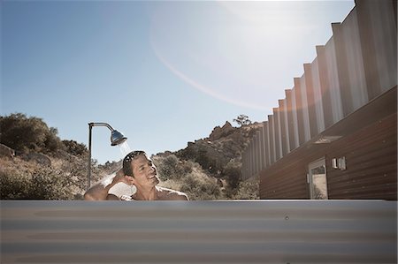 A man taking a shower outdoors on the terrace of a low impact eco house. Stock Photo - Premium Royalty-Free, Code: 6118-08393992