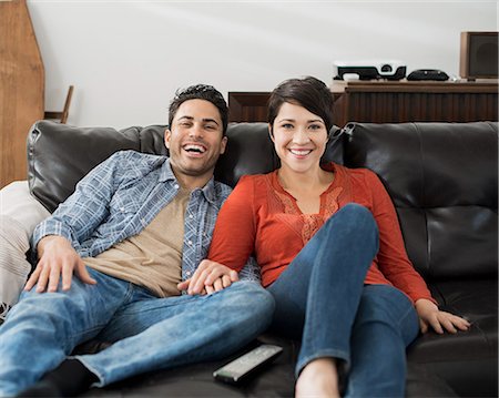 A man and woman sitting on a sofa, side by side, holding hands and watching a screen. Photographie de stock - Premium Libres de Droits, Code: 6118-08394042