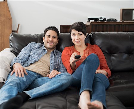 A man and woman sitting on a sofa, side by side, one using the remote control for the tv. Stock Photo - Premium Royalty-Free, Code: 6118-08394044