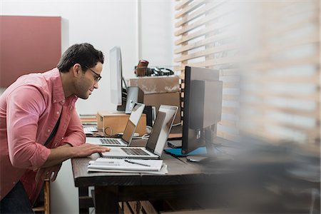 simsearch:6118-07966891,k - A man in a home office with a desk with two laptops, checking information on the screen. Photographie de stock - Premium Libres de Droits, Code: 6118-08394069