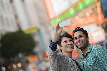 A couple, man and woman on a city street taking a selfy with a smart phone. Stock Photo - Premium Royalty-Free, Code: 6118-08394081