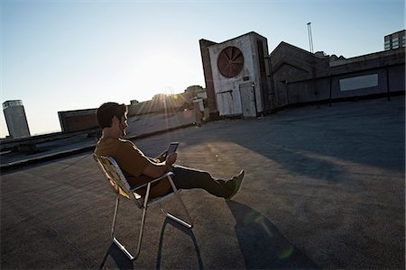 simsearch:6118-08394107,k - A man sitting in a beach chair on a city rooftop, using a digital tablet. Foto de stock - Sin royalties Premium, Código: 6118-08394090