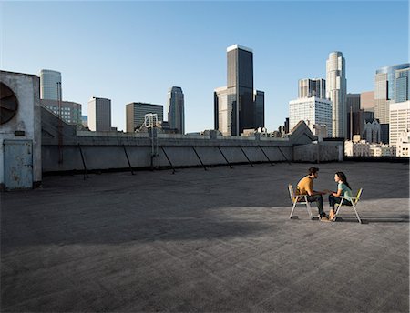 simsearch:6118-08394126,k - A couple, man and woman sitting in deck chairs on a rooftop overlooking city skyscrapers. Foto de stock - Sin royalties Premium, Código: 6118-08394092