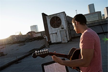 simsearch:6118-08394016,k - A man playing a guitar, sititng on a rooftop terrace overlooking the city at dusk. Foto de stock - Sin royalties Premium, Código: 6118-08394094