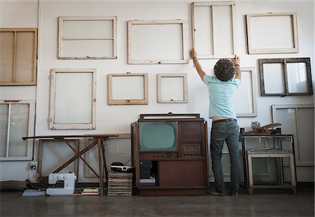 Loft decor. A man hanging framed picture canvases on a wall. Photographie de stock - Premium Libres de Droits, Code: 6118-08394025