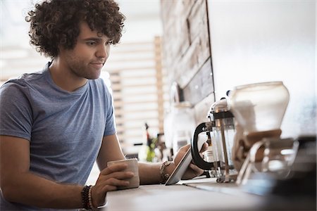 Loft living. A young man sitting with a cup of coffee, holding a digital tablet. Photographie de stock - Premium Libres de Droits, Code: 6118-08394033