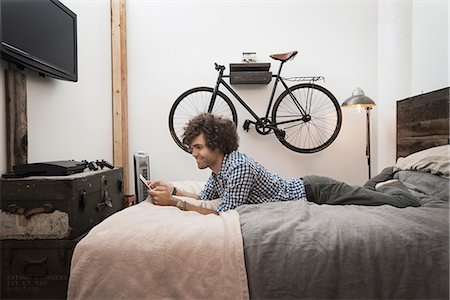 Loft living. A bicycle hanging on a wall. A man using a digital tablet. Stock Photo - Premium Royalty-Free, Code: 6118-08394031