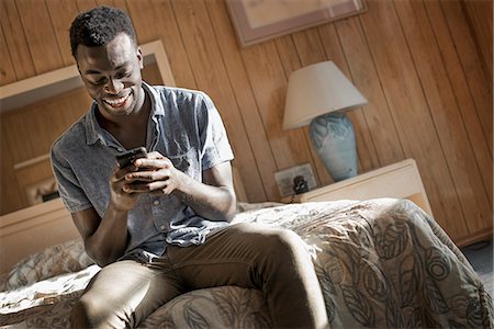 A young man in a motel room checking his smart phone. Stockbilder - Premium RF Lizenzfrei, Bildnummer: 6118-08394197