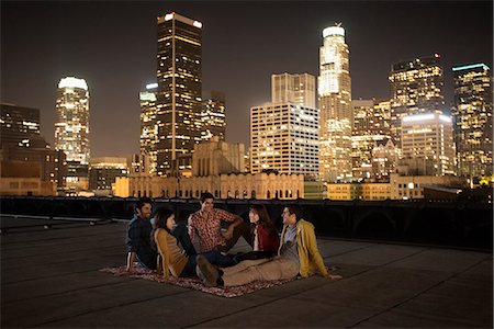 simsearch:6118-08394126,k - A group of friends gathered on a rooftop overlooking a city lit up at night. Foto de stock - Sin royalties Premium, Código: 6118-08394123