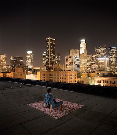 simsearch:6118-08394085,k - A man sitting on a rug on a rooftop overlooking a city lit up at night. Foto de stock - Sin royalties Premium, Código: 6118-08394121