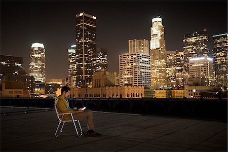 simsearch:6118-08394126,k - A man seated in a beach chair on a rooftop overlooking Los Angeles at night. Foto de stock - Sin royalties Premium, Código: 6118-08394125