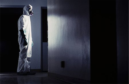 Man wearing a hazardous material protective clean suit, facing bright light in hallway Stock Photo - Premium Royalty-Free, Code: 6118-08399567