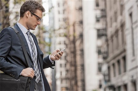 A working day. Businessman in a work suit and tie on a city street, using his phone. Stock Photo - Premium Royalty-Free, Code: 6118-08399583
