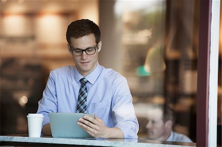 A working day. Businessman in a shirt and tie seated using a digital tablet in a cafe. Stock Photo - Premium Royalty-Free, Code: 6118-08399582