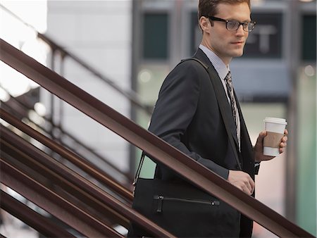 A working day. Businessman in a work suit and tie walking down steps holding a cup of coffee. Stock Photo - Premium Royalty-Free, Code: 6118-08399590