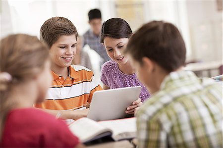 simsearch:6118-08351907,k - A group of students seated at a desk in a lesson talking to each other and sharing a digital tablet. Photographie de stock - Premium Libres de Droits, Code: 6118-08399646