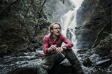 person looking up at sky clouds - A man sitting on a rock by a waterfall, holding a flask. Winter hiking. Photographie de stock - Premium Libres de Droits, Code: 6118-08399665