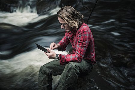 A man sitting by a fast flowing stream using a digital tablet. Photographie de stock - Premium Libres de Droits, Code: 6118-08399669